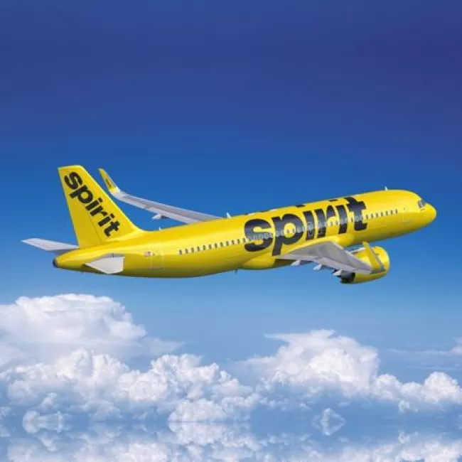 A Spirit Airlines airplane soars through blue skies.